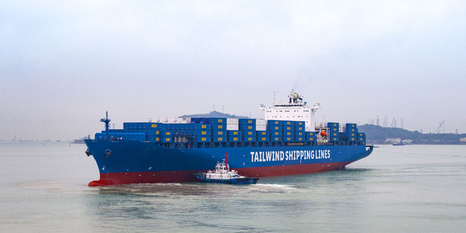 Tailwind Shippinglines container ship on the water in front of a port.