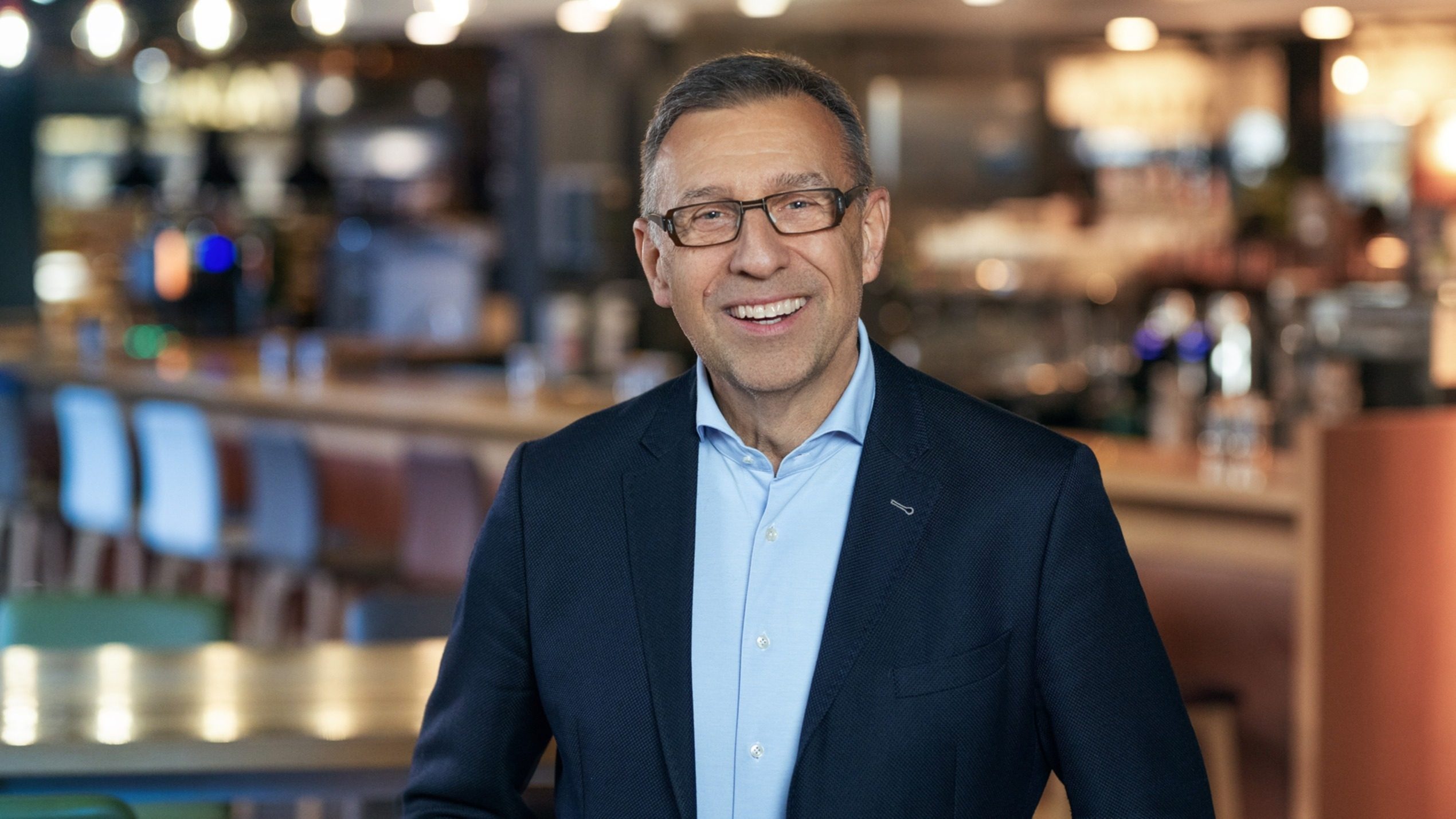 Der Mitarbeiter der Schwarz Gruppe Gerd Rinkenauer lacht in die Kamera. Im Hintergrund ist ein Restaurant zu erkennen.