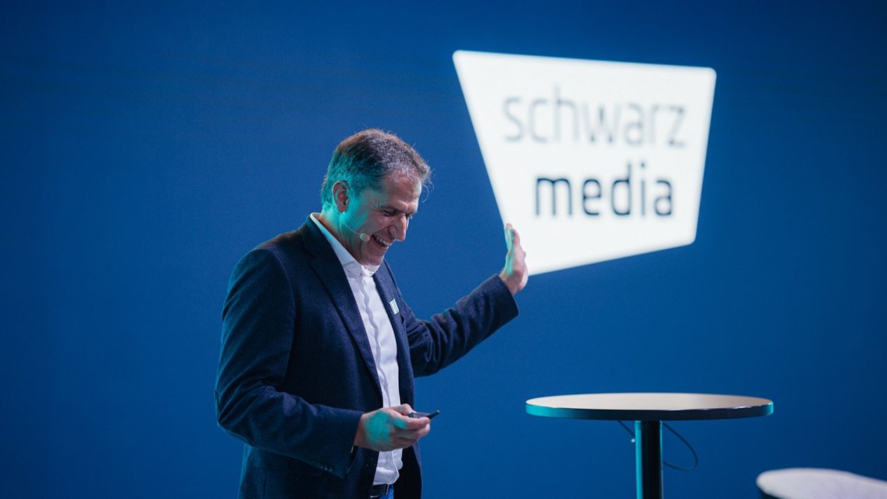 Lachender Mann der auf das Schwarz Media Logo zeigt