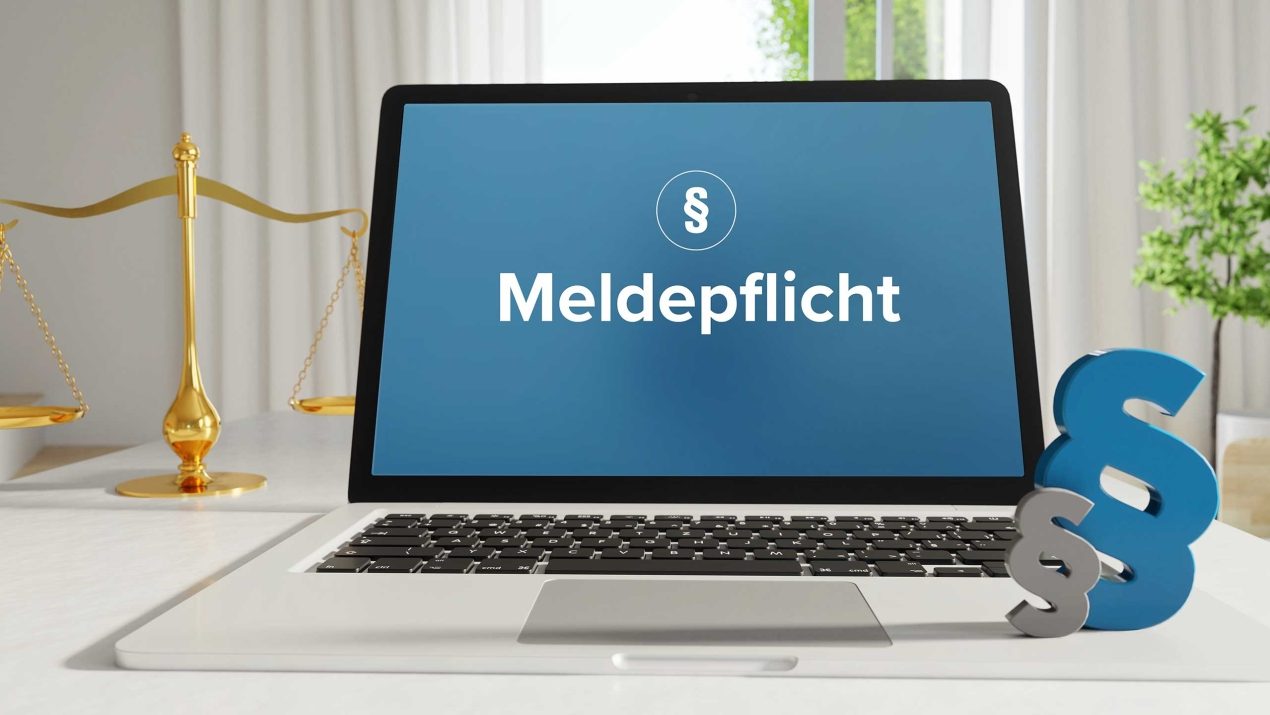 Laptop displaying the word Meldepflicht (reporting obligation) alongside a golden scale and paragraph symbols, representing legal compliance and statutory requirements.