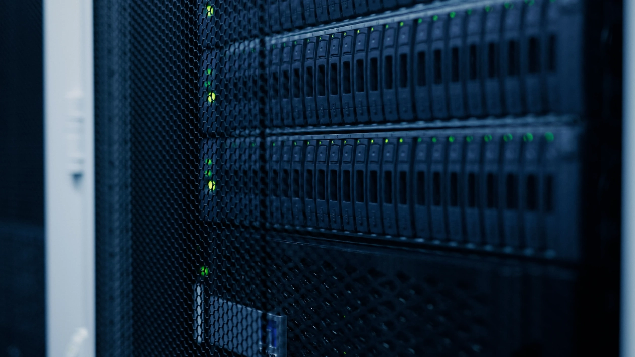 Close-up of server racks featuring multiple hard drive bays and blinking green status LED lights in a data center located, viewed through a black mesh enterprise cabinet door.