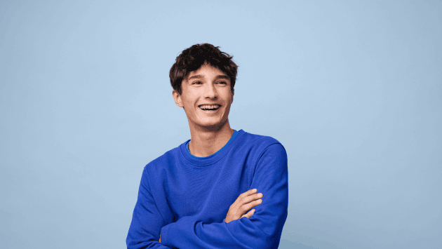Junger Mann mit blauem Pulli vor hellblauem Hintergrund lacht