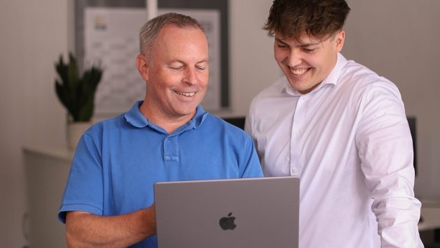 Ein Ausbilder erklärt einem Auszubildenden etwas am Laptop.