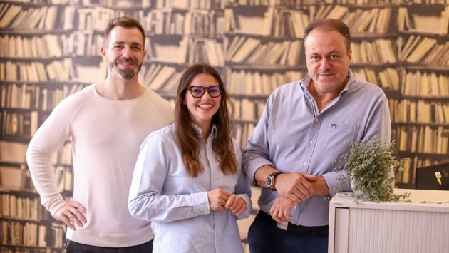 Drei Mitarbeiter stehen nebeneinander und lächeln in die Kamera.