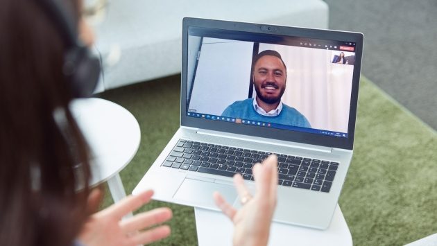 Über der Schulter eine Mitarbeiterin ist ein Laptop mit geöffnetem Teamsfenster zu sehen. Darauf ist ein Mitarbeiter, der in Kamera lacht.