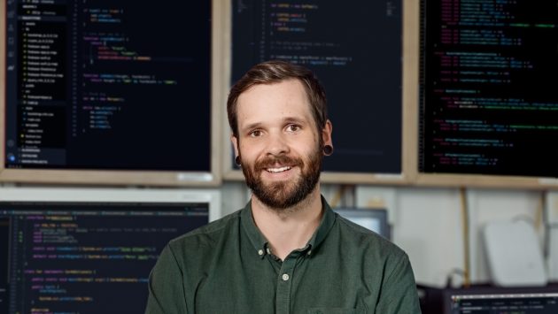 Ein Mitarbeiter der IT steht vor vielen Bildschirmen, auf denen IT-Codes zu sehen sind.