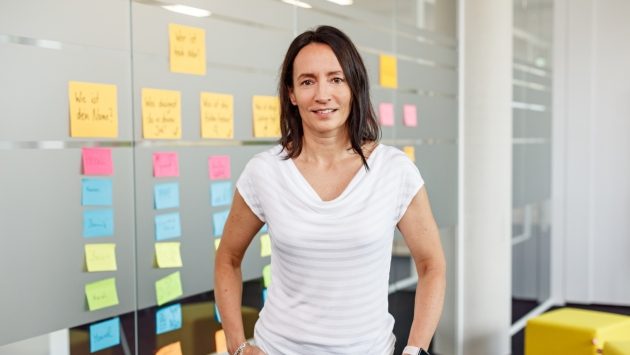 Eine Mitarbeiterin der SIT steht vor einer Glasfront, auf der viele bunte Post-Its zu sehen sind.