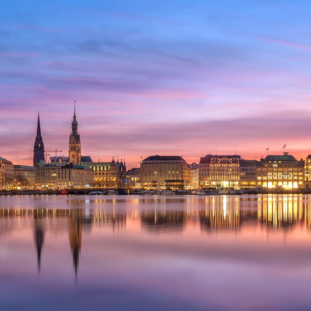 Panoramic view of Hamburg's Inner Alster lake at dusk with an illuminated skyline reflecting in calm water.