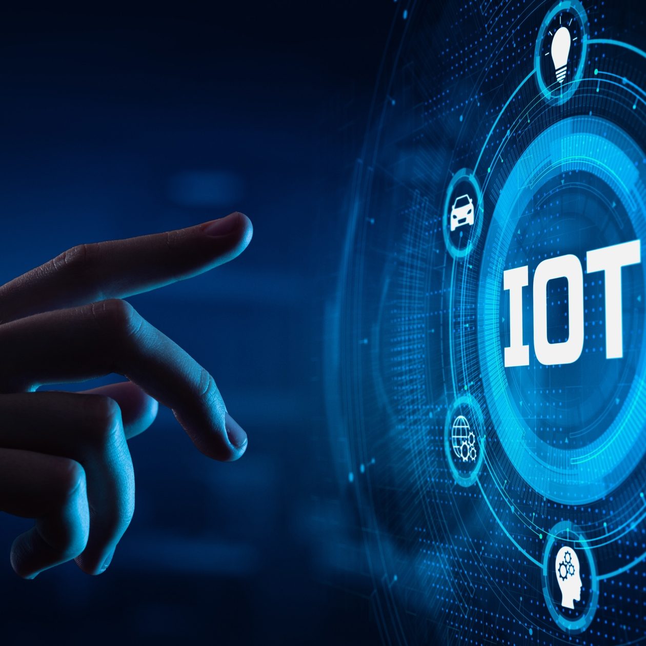 Eine menschliche Hand berührt ein futuristisches, leuchtend blaues Digital-Display mit dem zentralen Schriftzug IOT (Internet of Things). Um das IOT-Symbol sind Icons angeordnet, die vernetzte Geräte wie Auto, Haus, Sensor und Kopf (Künstliche Intelligenz) symbolisieren. Das Bild veranschaulicht die digitale Vernetzung im Zeitalter des Internet der Dinge.