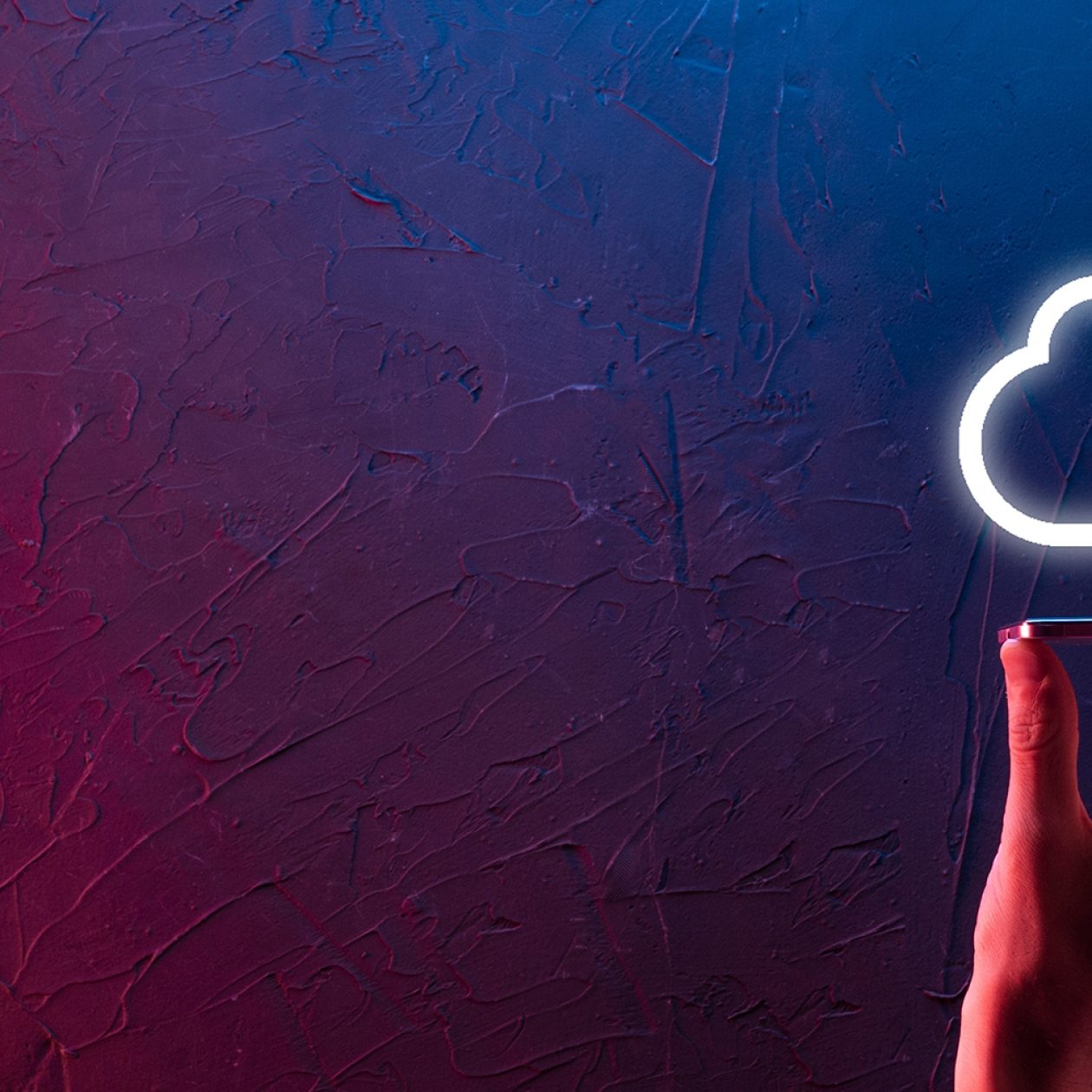Eine Hand hält ein Smartphone oder Tablet, über dem ein leuchtendes, neonfarbenes Wolken-Symbol (Cloud) schwebt. Die Szene ist dramatisch in rot-blauen Farbtönen beleuchtet und symbolisiert Cloud Computing, Datenspeicherung und digitale Technologie.