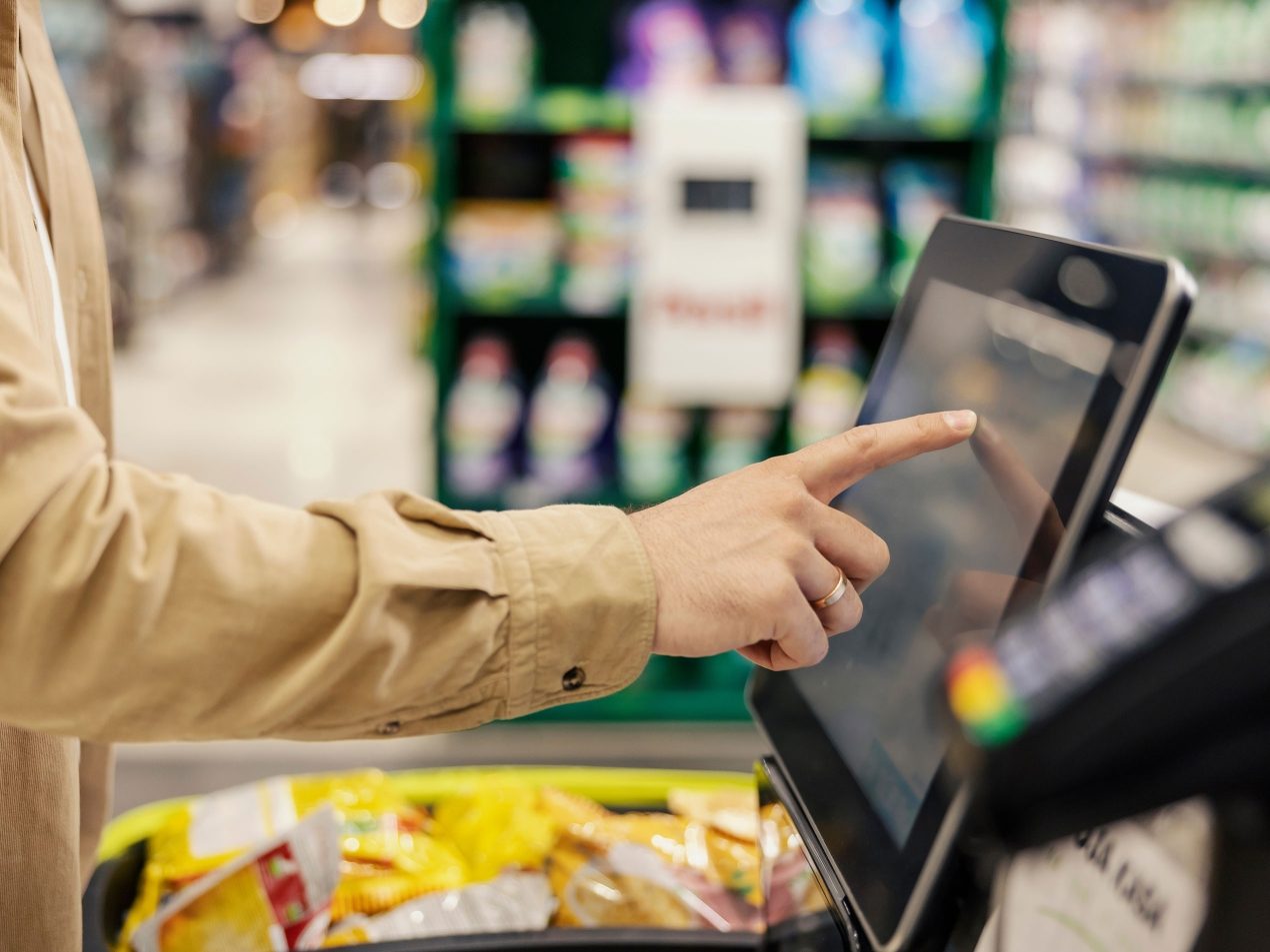 Kunde bedient den Touchscreen einer Self-Checkout-Kasse (SB-Kasse) im Supermarkt beim Lebensmitteleinkauf.