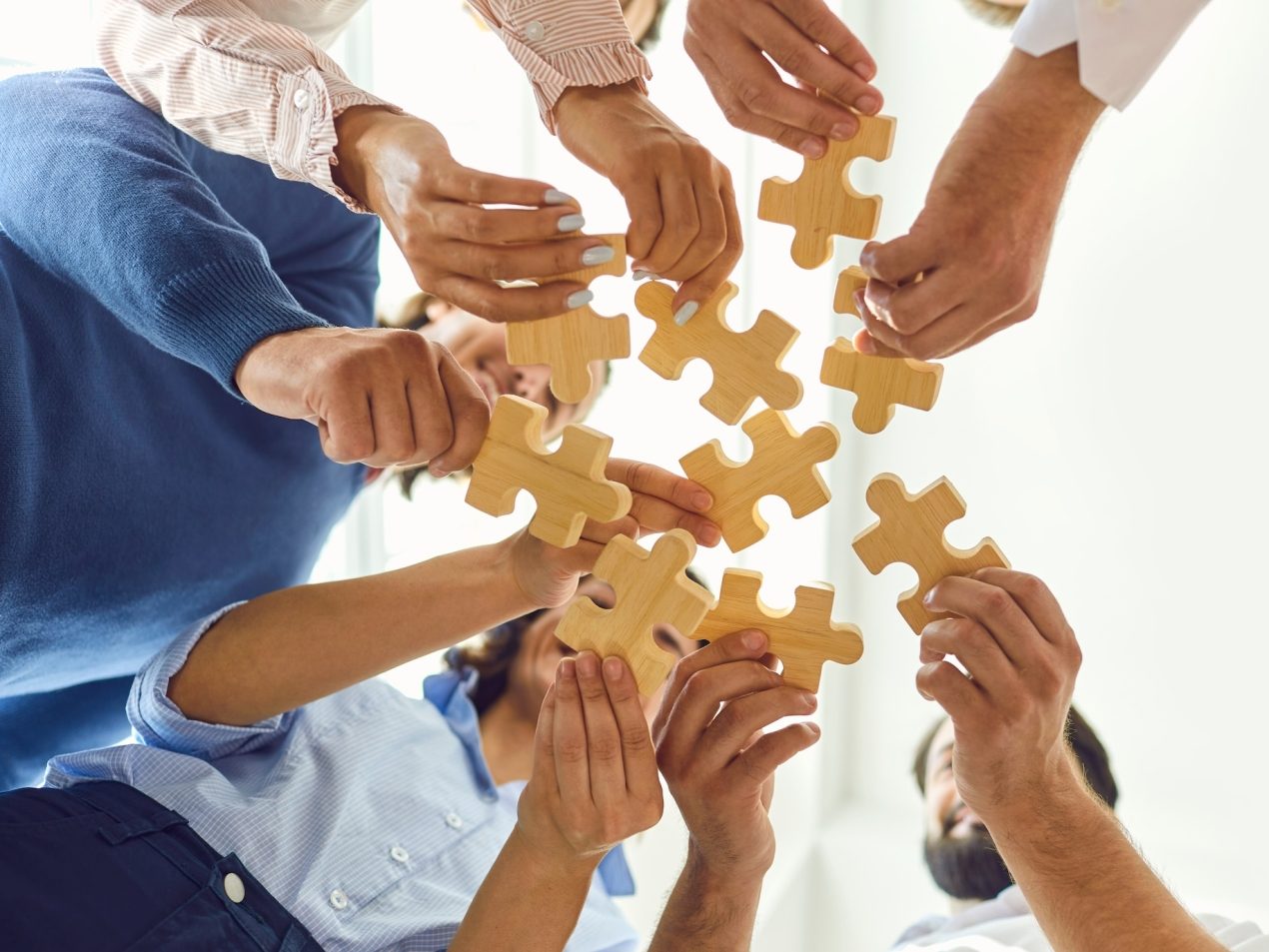 Viele Hände die Puzzleteile halten und zusammen stecken