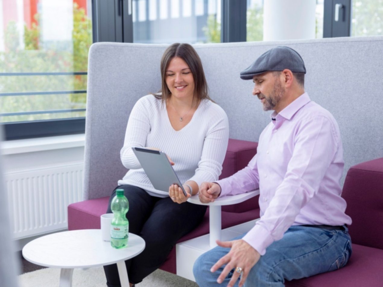 Zwei Mitarbeiter sitzen in einer Besprechungslounge und tauschen sich an einem Tablet aus.