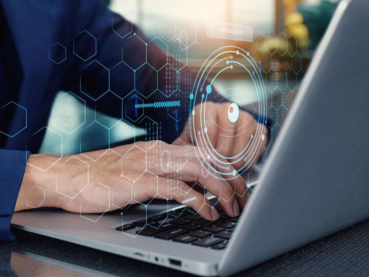 Hände tippen auf einem Laptop, über dem eine futuristische, leuchtende Benutzeroberfläche mit einem Cybersicherheits-Schriftzug und einem Zielkreis zur Datenverschlüsselung projiziert ist. Symbolisiert IT-Sicherheit und digitale Abwehr.