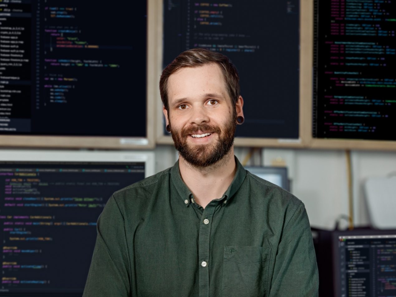 Ein Mitarbeiter der IT steht vor vielen Bildschirmen, auf denen IT-Codes zu sehen sind.