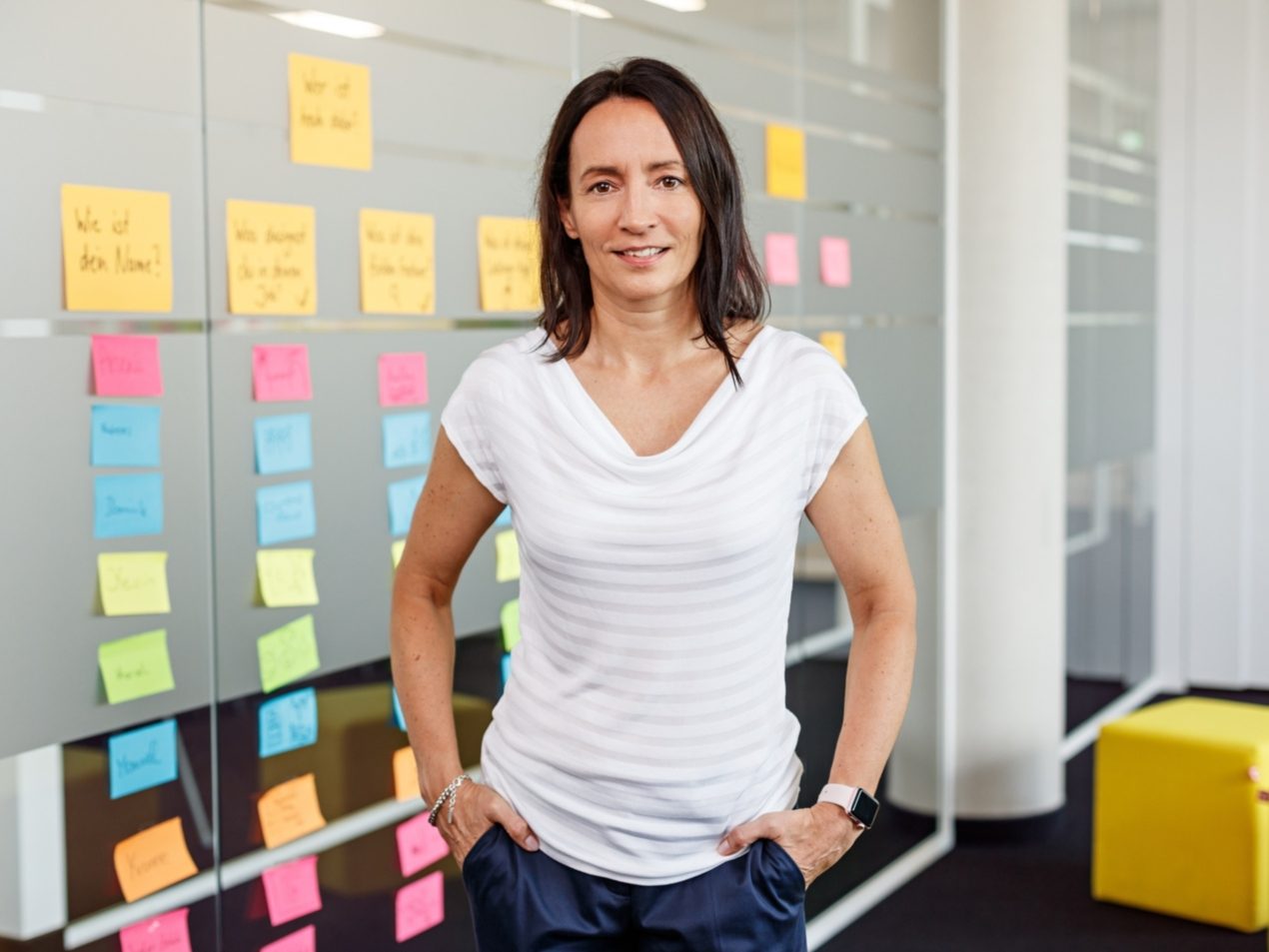 Eine Mitarbeiterin der SIT steht vor einer Glasfront, auf der viele bunte Post-Its zu sehen sind.