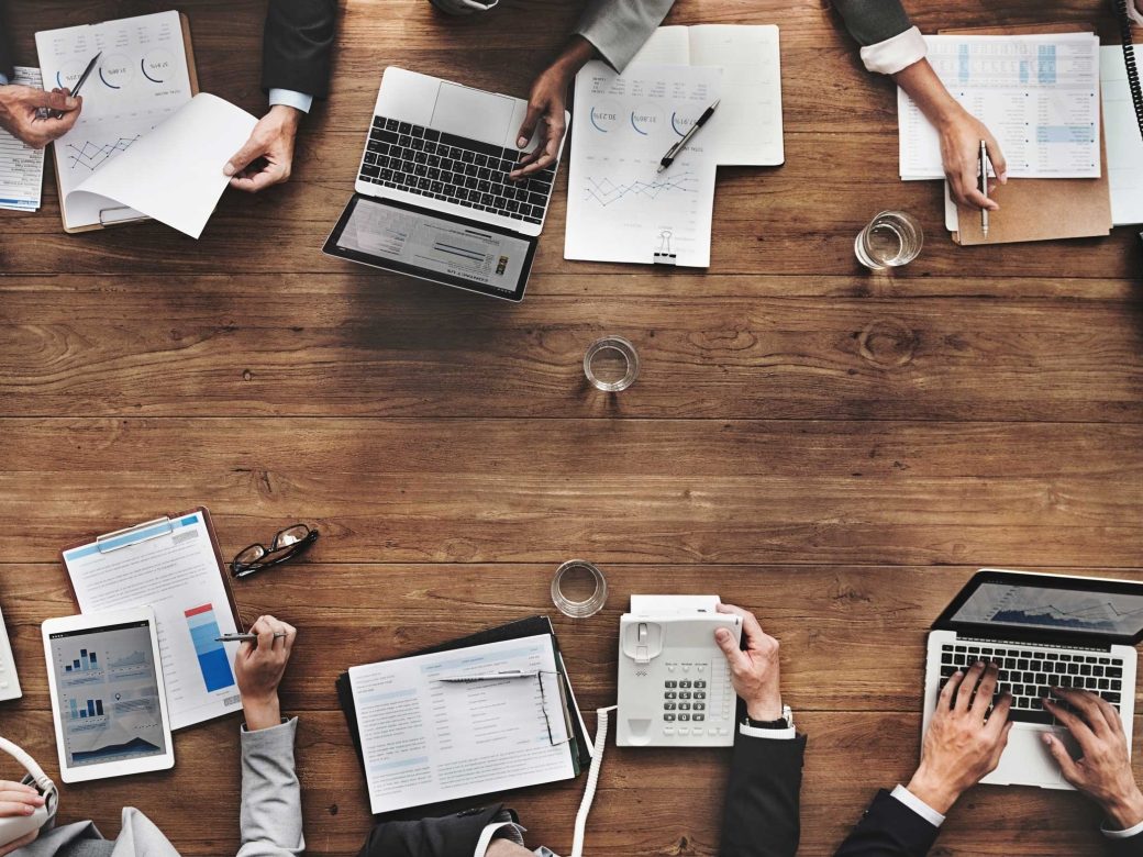 Team in der Geschäftsanalyse (Überkopfansicht). Auf dem Tisch liegen Finanzberichte, Grafiken und technische Geräte.