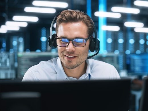 IT support employee with customer service headset works concentrated in front of the background of a server room.