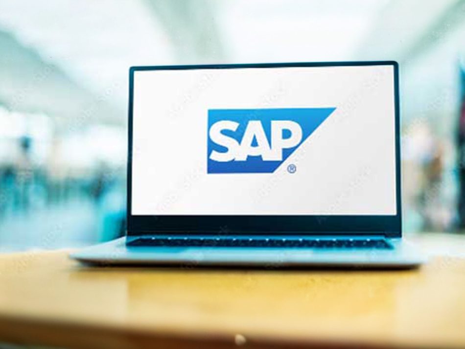 Laptop mit aufgeklapptem Bildschirm, auf dem prominent das blaue SAP-Logo (weiß stilisierte Buchstaben "SAP" in einem blauen Rechteck mit einer diagonalen Linie) auf weißem Hintergrund zu sehen ist. Das Bild zeigt das Notebook auf einem Tisch, mit unscharfem (Bokeh-)Hintergrund, der eine moderne Büro- oder Geschäftsumgebung andeutet. Eignet sich zur Bebilderung von Themen wie Enterprise-Resource-Planning (ERP), Software, Business-Technologie oder dem Unternehmen SAP.