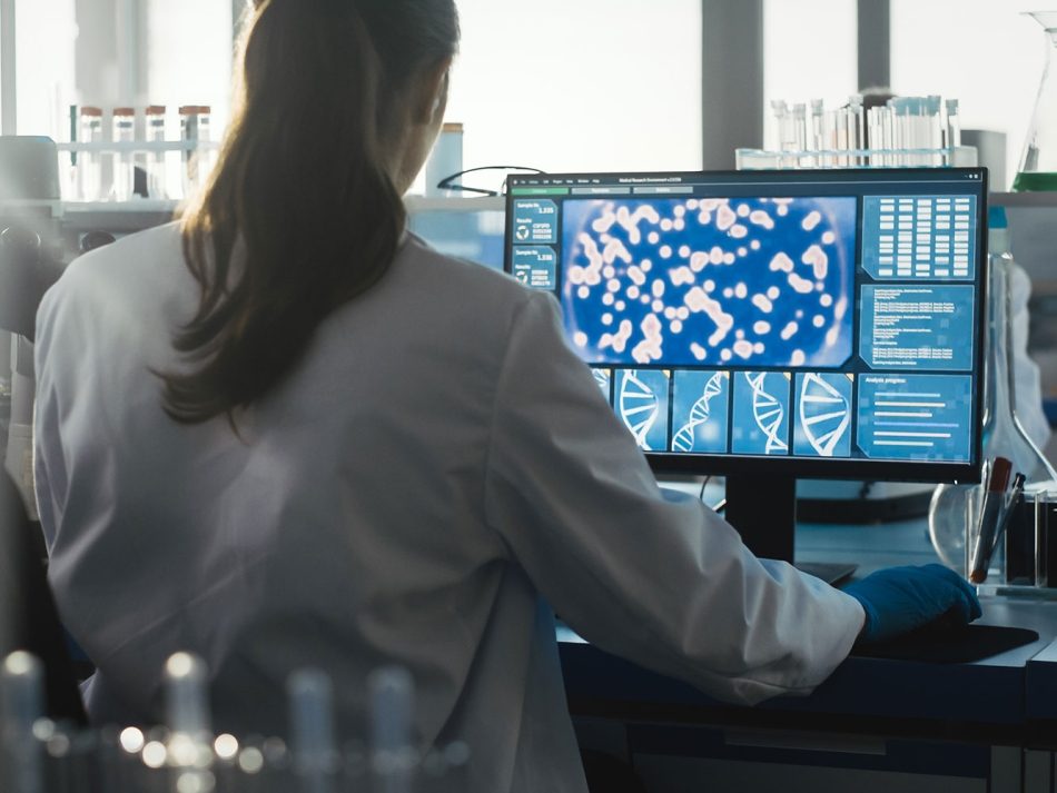 Scientist analyzing microscopic data and DNA sequences on a monitor for drug target discovery in a laboratory.