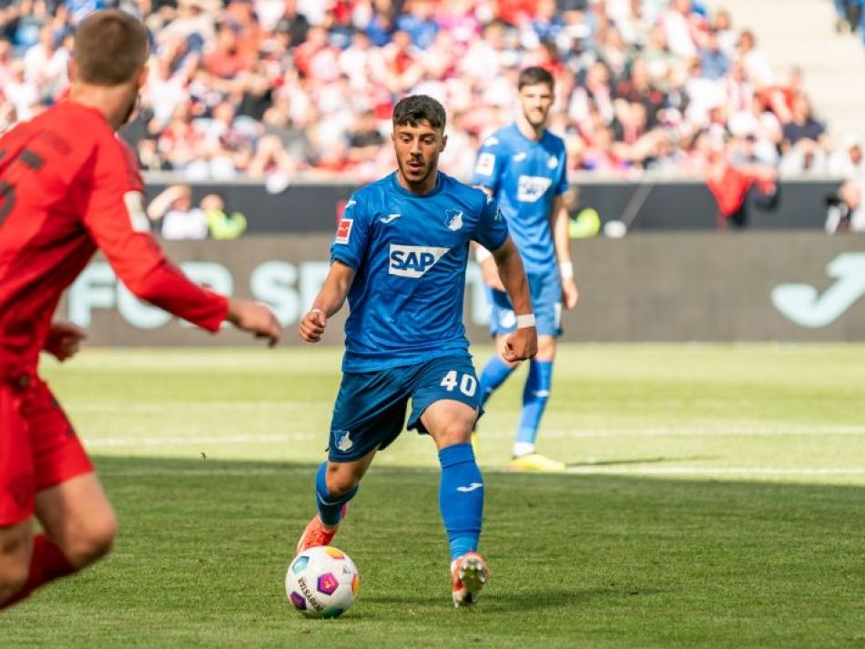 Fußballspieler der TSG Hoffenheim (blaues Trikot mit Nummer 40, SAP-Sponsor) am Ball, dribbelnd auf dem Spielfeld während eines Bundesligaspiels. Ein gegnerischer Spieler im roten Trikot ist links im Bild zu sehen.