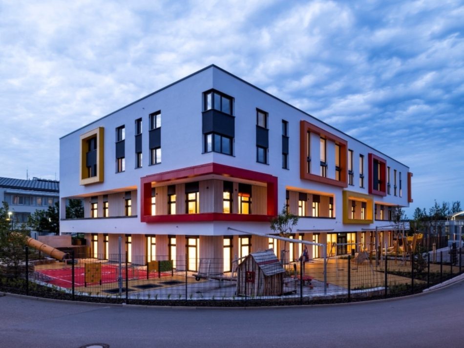 Eine moderne Kindertagesstätte von außen in der Dämmerung.