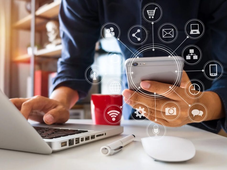 Person mit Smartphone in der einen Hand und mit der anderen Hand auf der Laptop Tastatur tippend