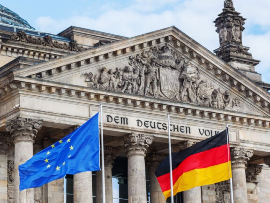 Die Fassade des Reichstagsgebäudes in Berlin mit der Inschrift "DEM DEUTSCHEN VOLKE" und wehenden Flaggen der Europäischen Union (EU) und Deutschlands. Das Bild symbolisiert deutsche Politik, den Deutschen Bundestag, Demokratie und die deutsch-europäische Zusammenarbeit.