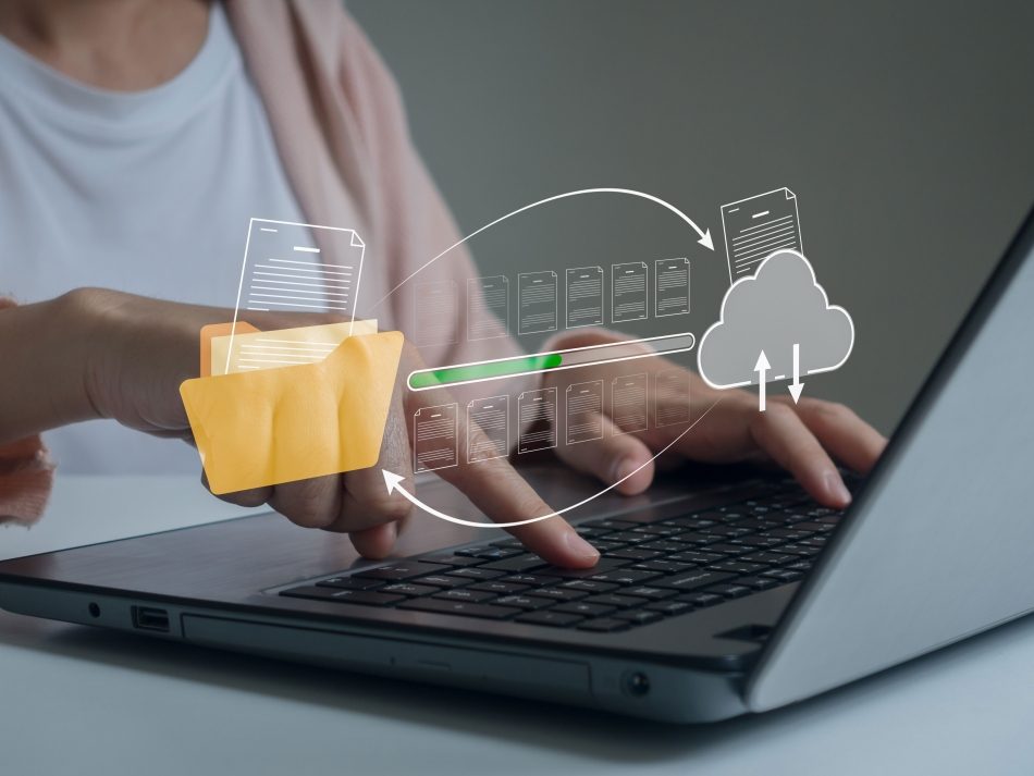 A person is typing on a laptop while a digital data flow is displayed from a yellow folder icon with a progress bar to a cloud icon. The image visualizes data upload, data backup, data migration and the transfer of documents to cloud storage.
