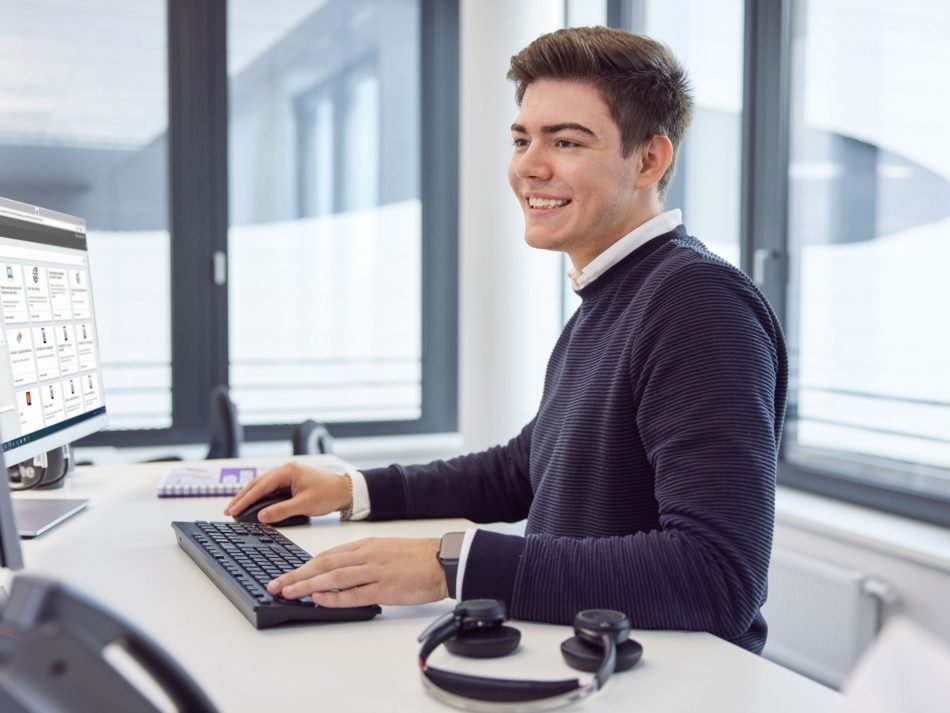 Ein Auszubildender steht an seinem Schreibtisch an seinem Arbeitsplatz.