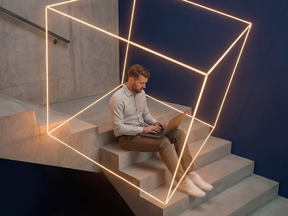 Ein Mann sitzt auf einer Betontreppe und arbeitet an einem Laptop, während er von einem leuchtenden, orangefarbenen geometrischen Würfel aus Lichtlinien umgeben ist.