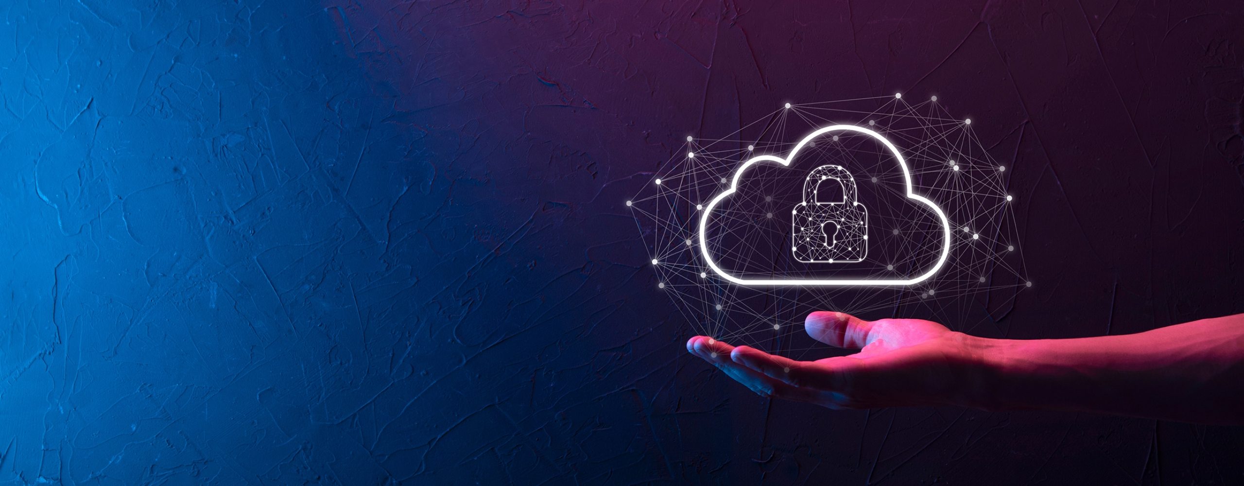 Eine Hand hält eine schwebende, leuchtend weiße Cloud-Grafik mit einem Vorhängeschloss-Symbol im Inneren. Die Cloud ist von einem digitalen Netzwerk aus Punkten und Linien umgeben. Der Hintergrund ist eine dunkle Wand, beleuchtet von blauem und pinkem Neonlicht. Das Bild symbolisiert Cloud-Sicherheit, Datenschutz und den Schutz digitaler Infrastrukturen.