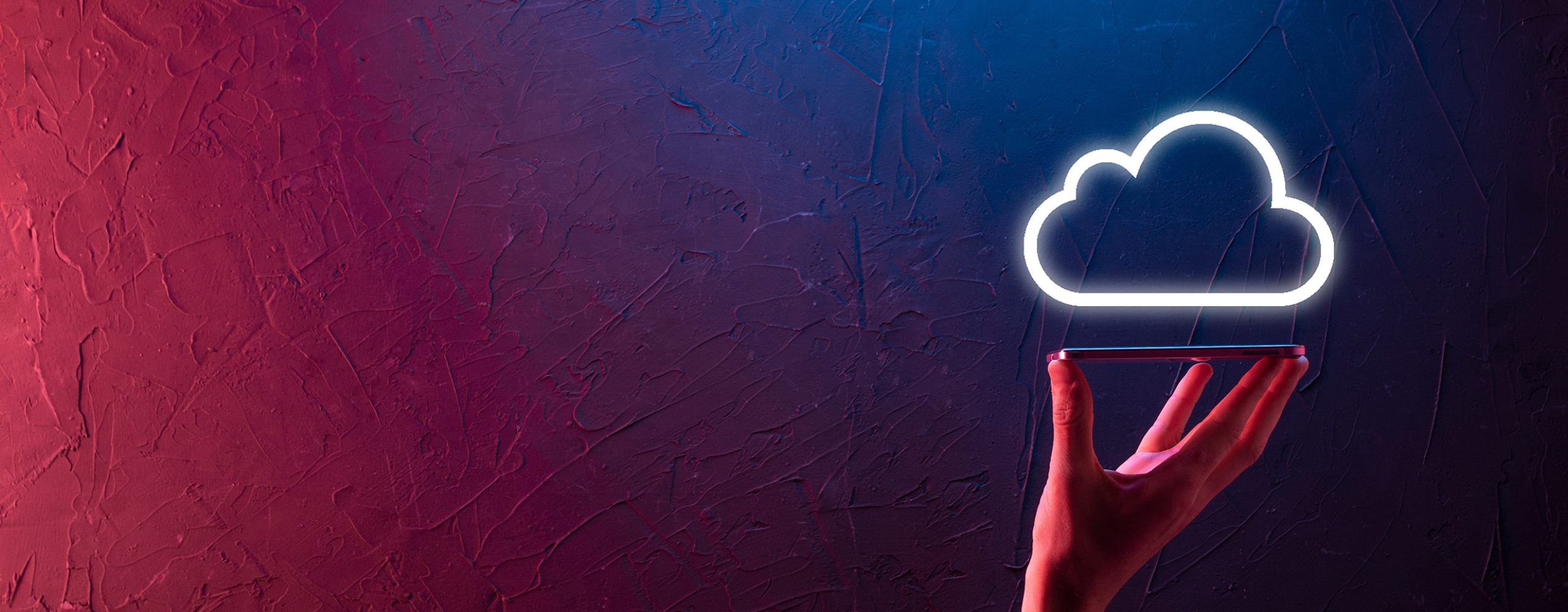Eine Hand hält ein Smartphone oder Tablet, über dem ein leuchtendes, neonfarbenes Wolken-Symbol (Cloud) schwebt. Die Szene ist dramatisch in rot-blauen Farbtönen beleuchtet und symbolisiert Cloud Computing, Datenspeicherung und digitale Technologie.