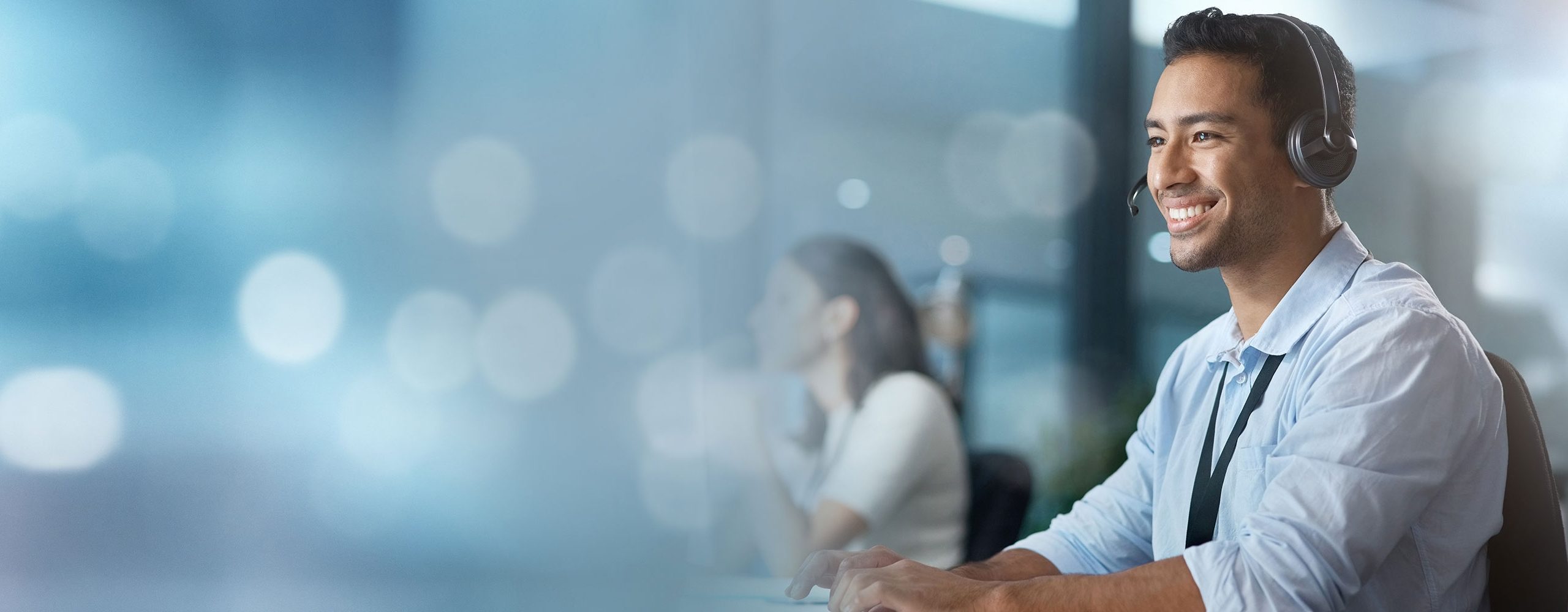 Smiling employee in a call center or service center, wearing a headset and working on a computer. Symbolizes professional customer support and client care.