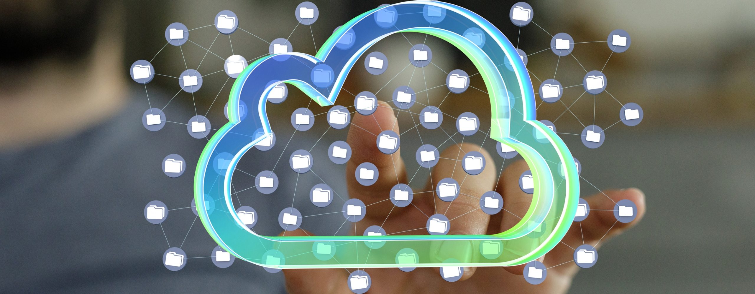 Close-up of a hand holding a glowing, futuristic cloud icon surrounded by a network of connected data points and folder icons. The image visualizes the concept of cloud computing for data storage, network integration and digital services.
