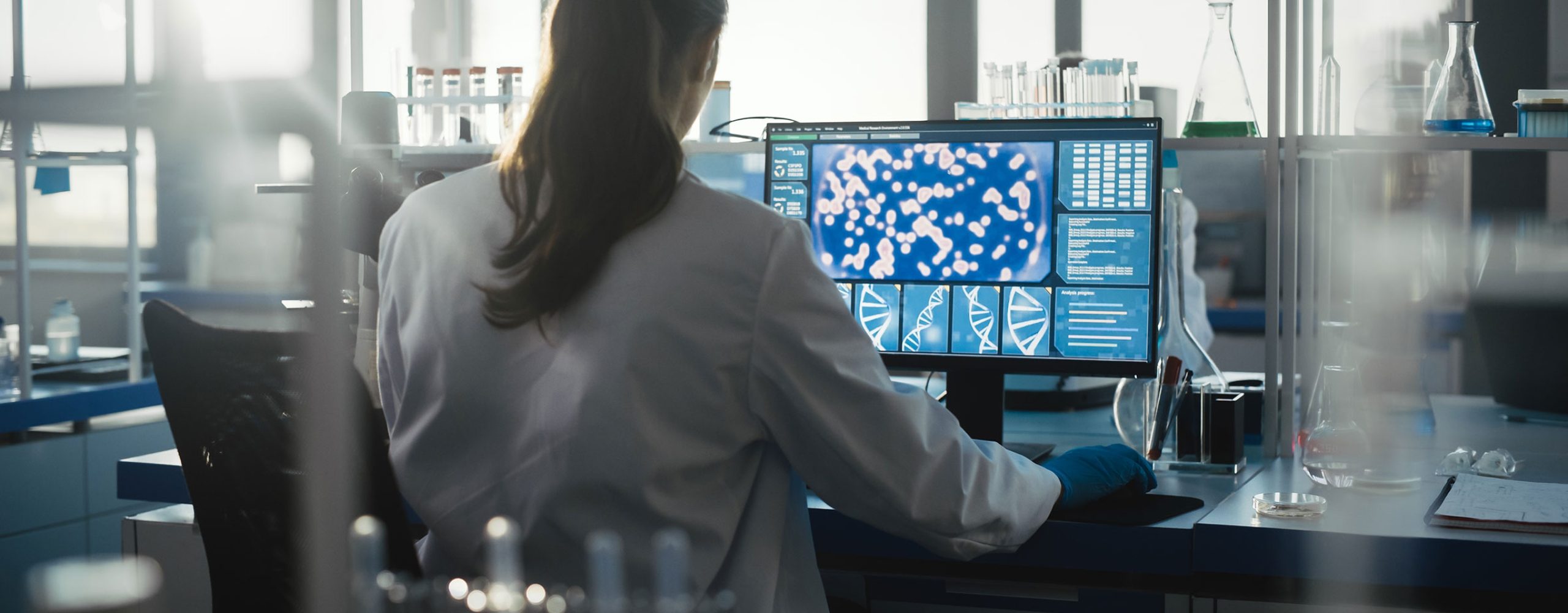 Scientist analyzing microscopic data and DNA sequences on a monitor for drug target discovery in a laboratory.