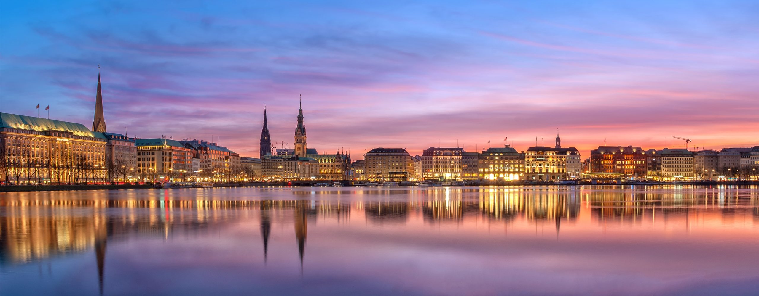 Panorama der Hamburger Binnenalster bei Dämmerung mit beleuchteter Skyline und Spiegelungen im ruhigen Wasser.